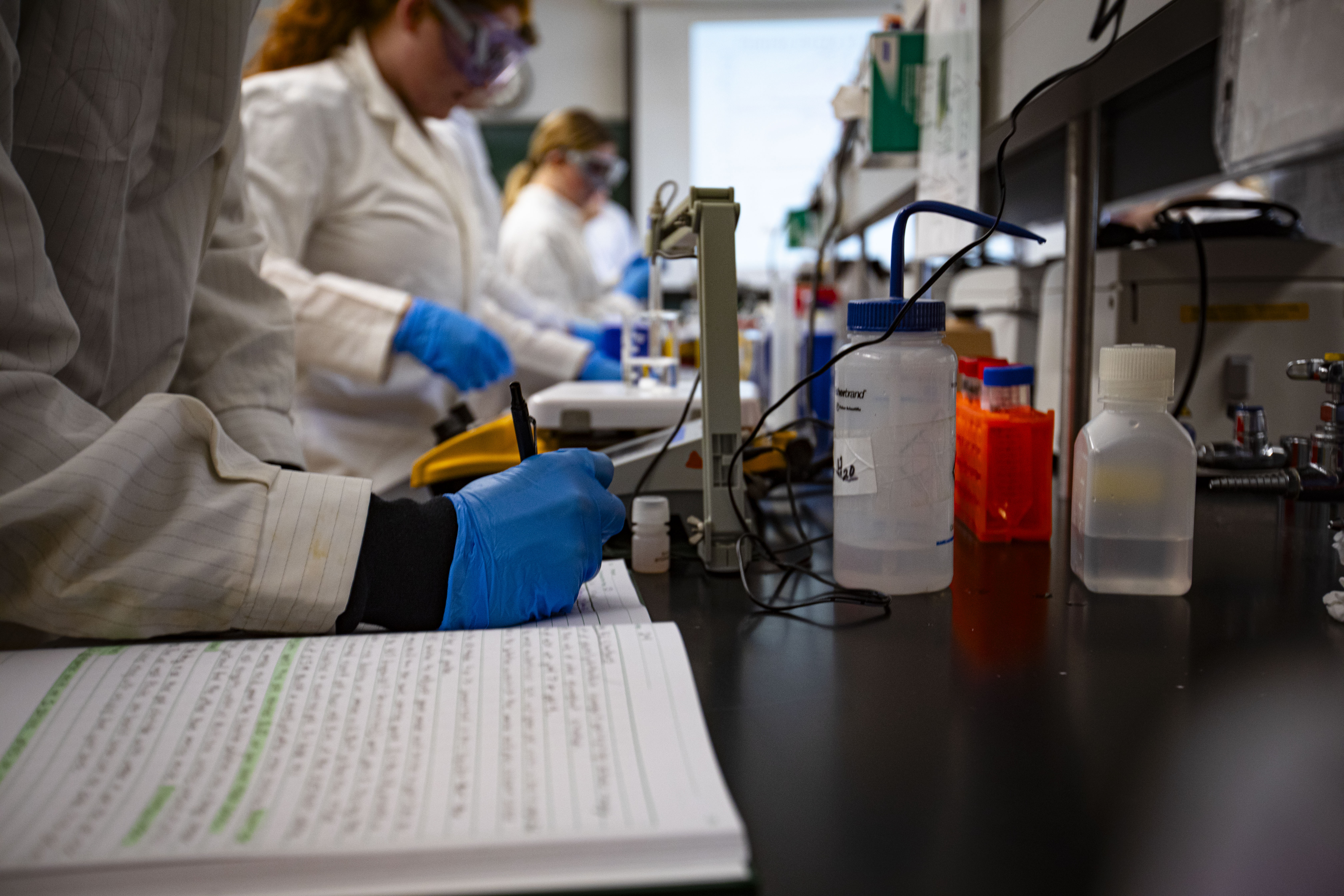 A person with gloves writes in a notebook in a lab
