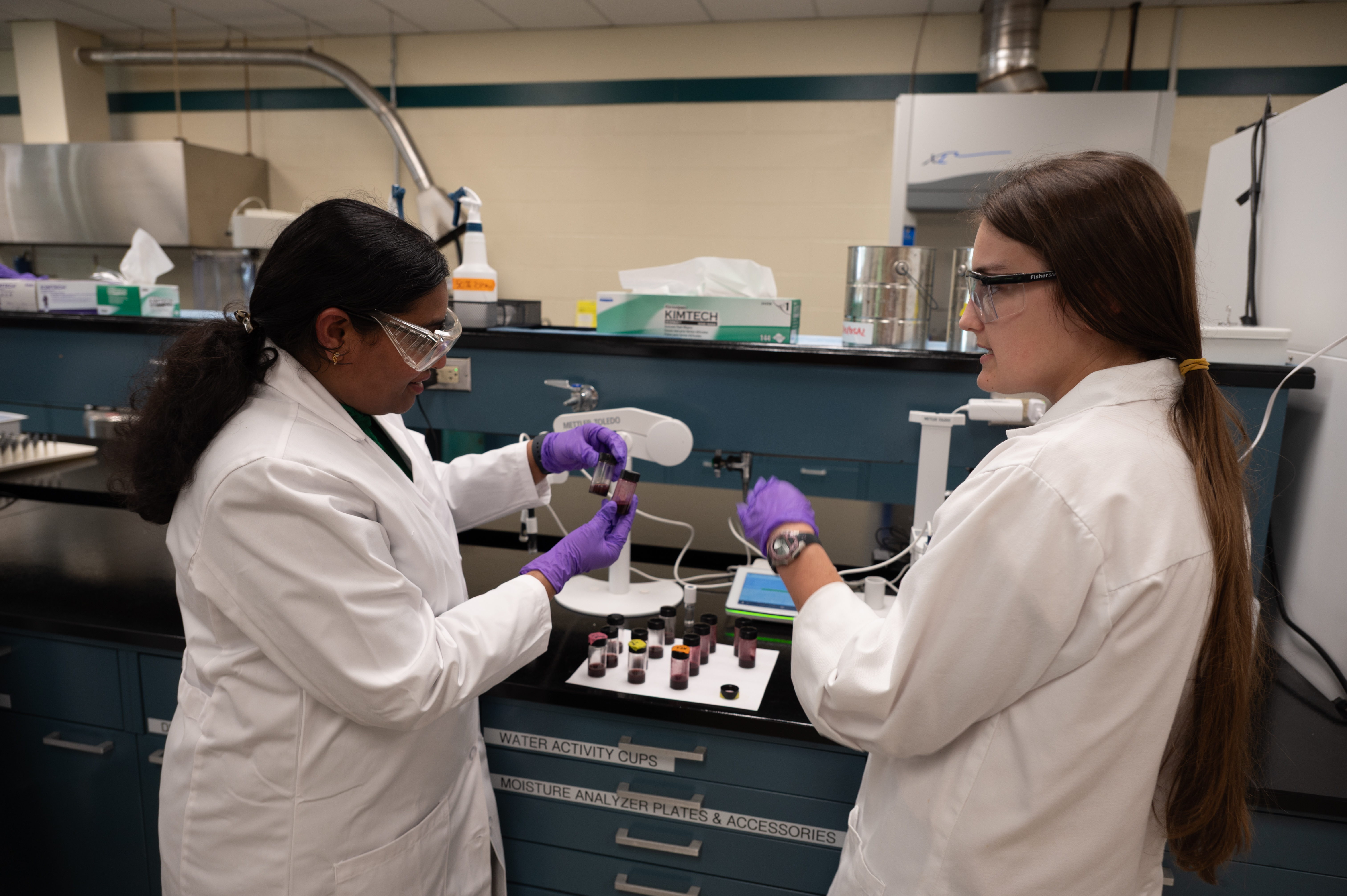 Dr. Kiruba and a student hold up small containers in a lab
