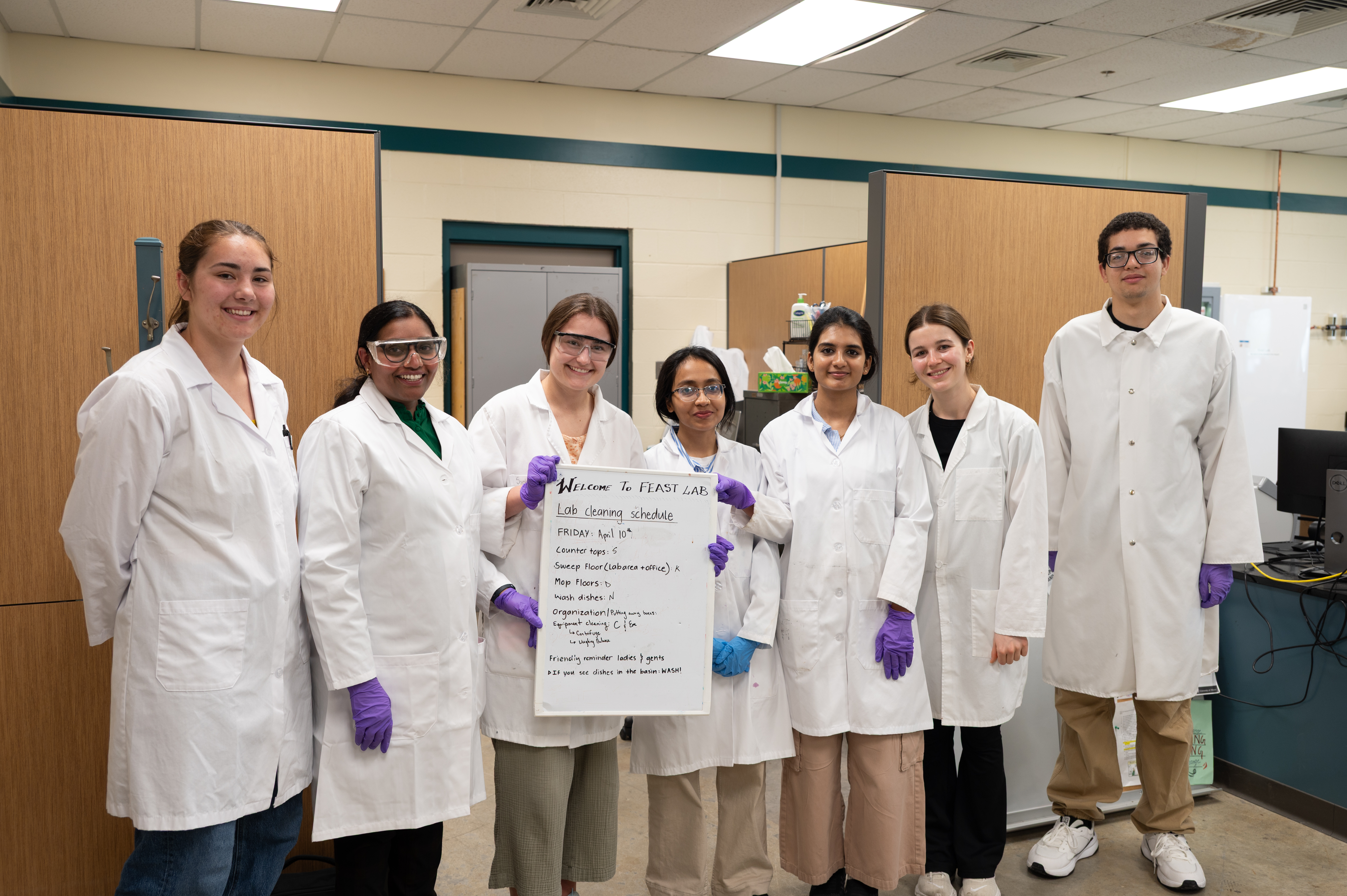 Dr. Kiruba and several of her students hold up a sign showing their lab cleaning schedule